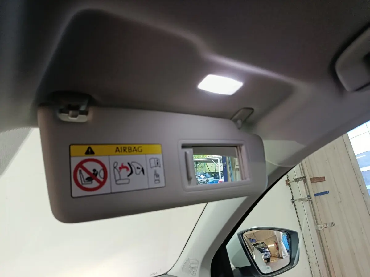 Vue intérieure du pare-soleil côté conducteur avec miroir et lumière, rétroviseur extérieur visible, couleur claire.