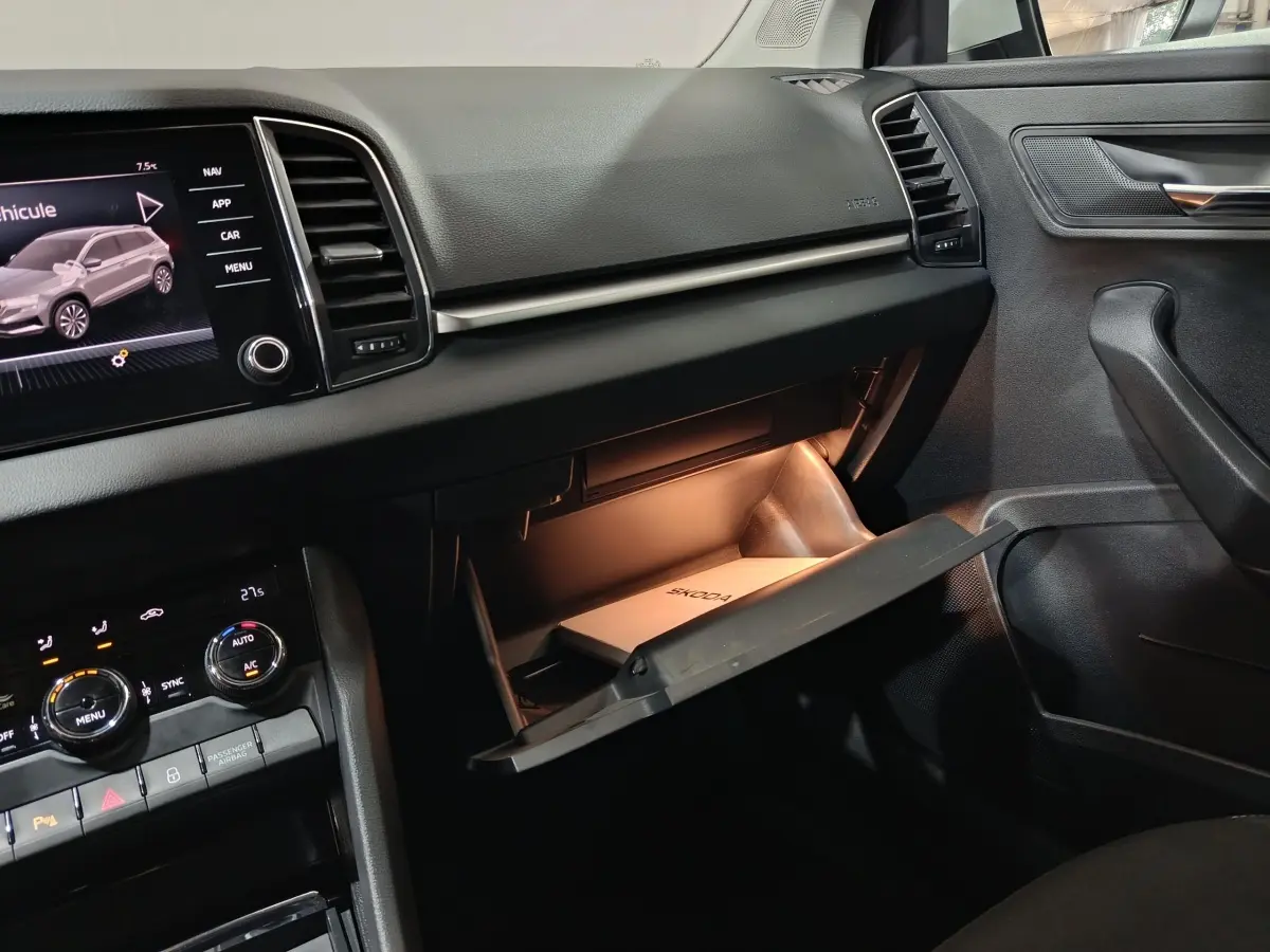 Intérieur noir du Skoda Karoq 2024, vue côté passager avec boîte à gants ouverte et écran tactile central allumé.