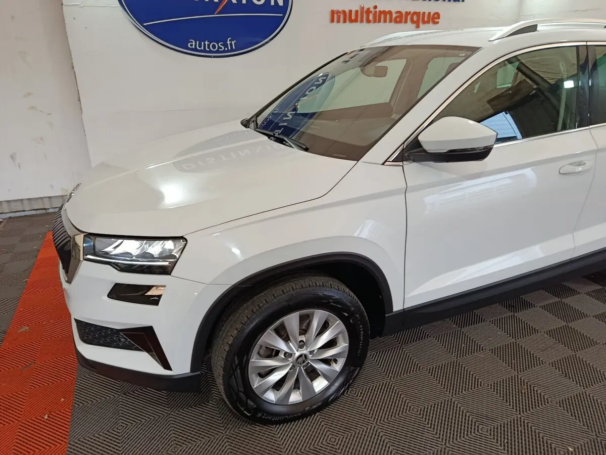 Vue 3/4 avant droit d'un Skoda Karoq blanc avec jantes alliage et phares LED dans un showroom.