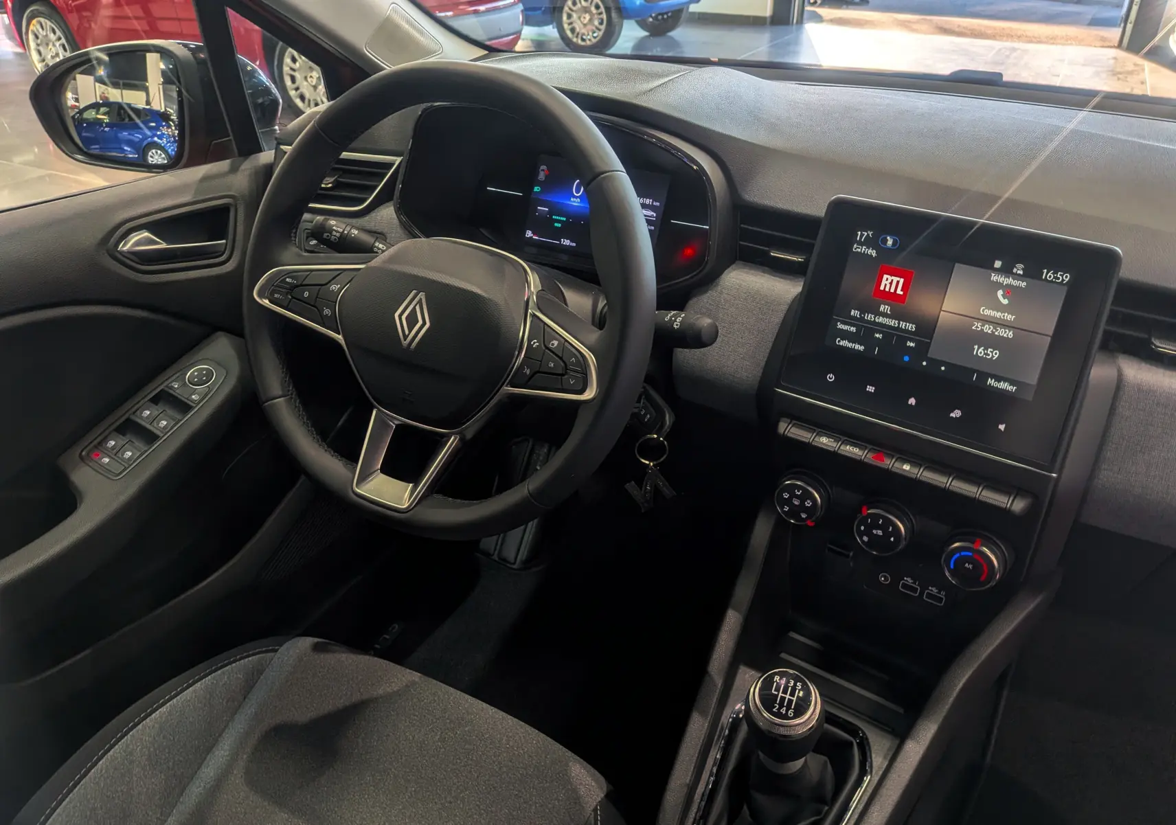 Vue intérieure côté conducteur de la Renault Clio V 2024, volant multifonction et écran tactile central allumé.