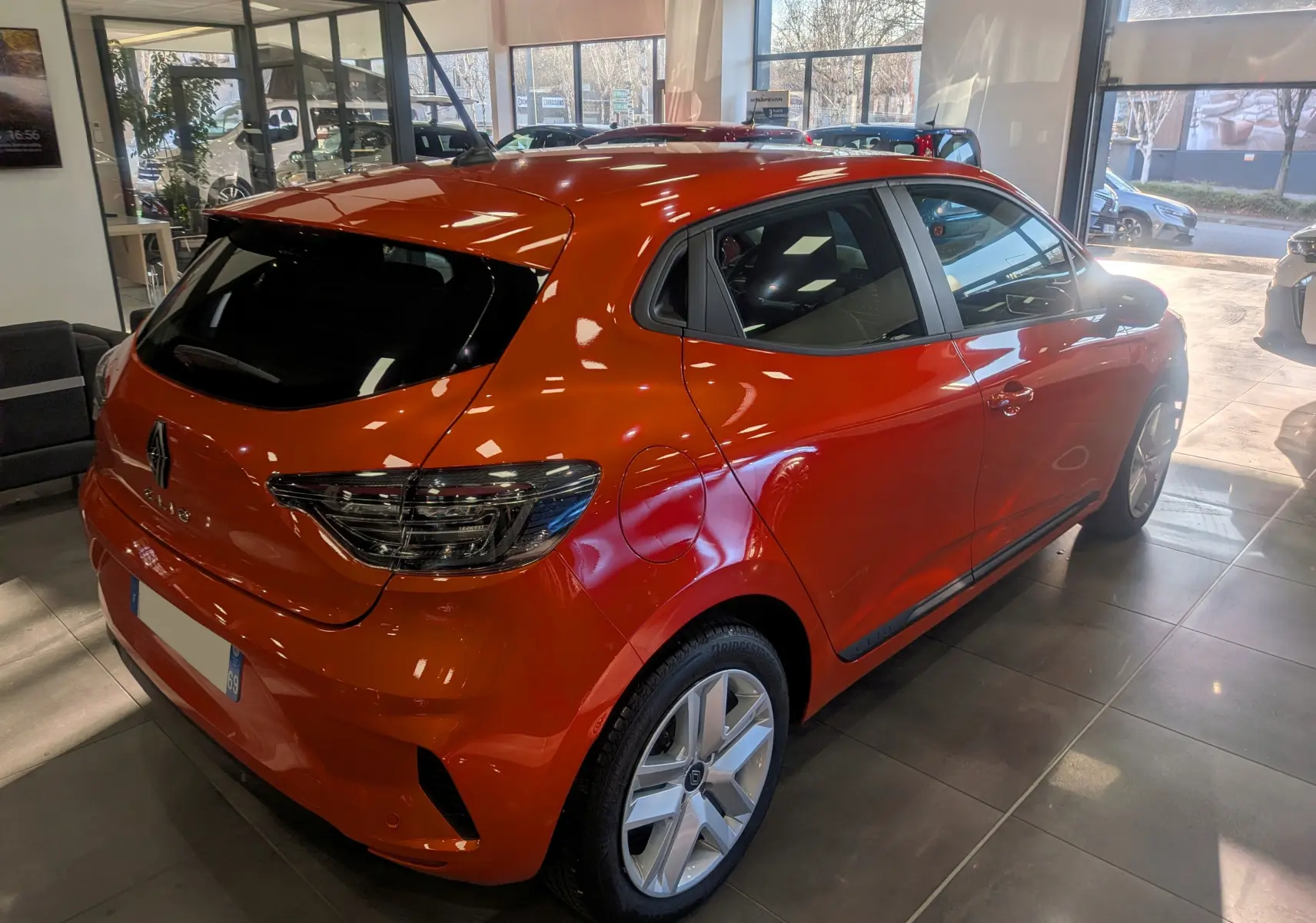 Vue 3/4 arrière droite d'une Renault Clio V Orange Valencia 2024 en showroom, avec feux arrière LED et jantes alliage.