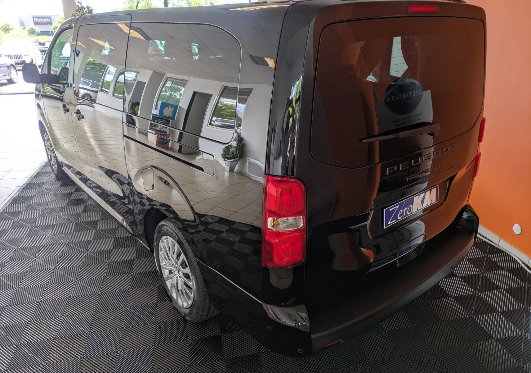 Vue 3/4 arrière gauche d'un Peugeot Traveller noir 2026, grand van avec vitres latérales teintées et feux arrière rouges.