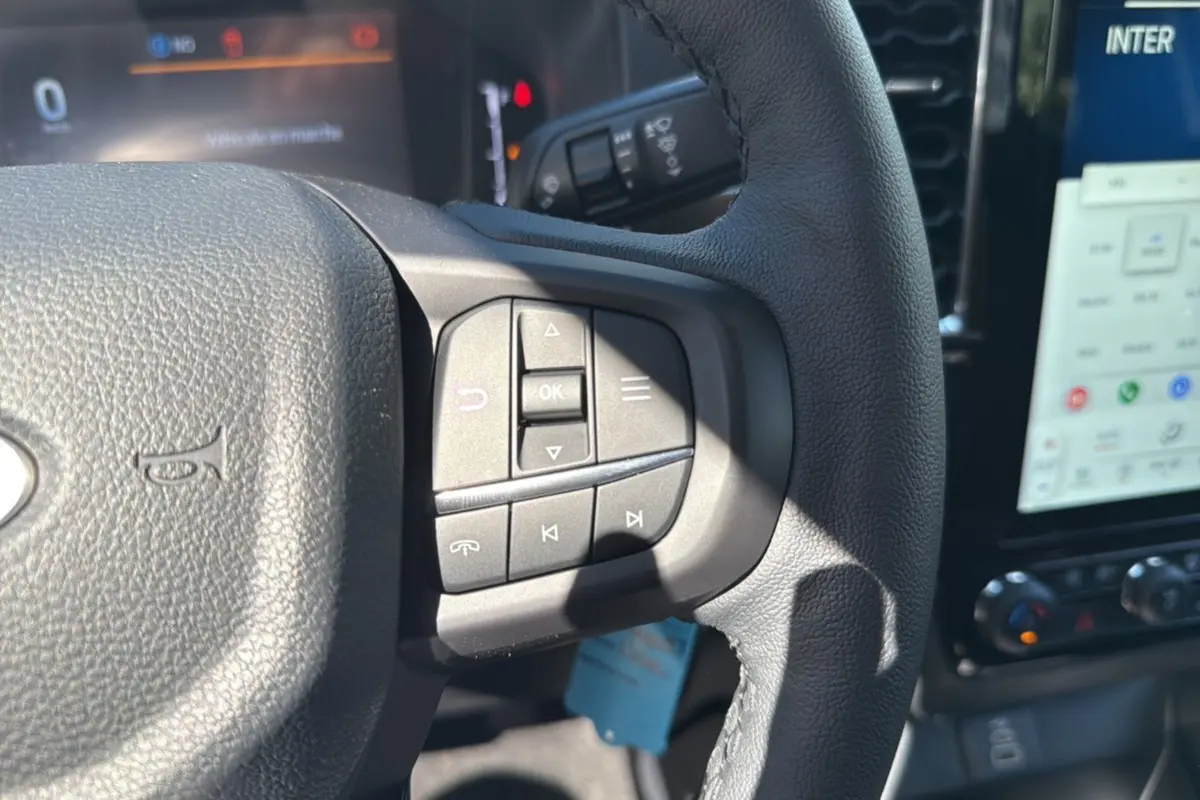 Gros plan sur le volant cuir multifonctions du Ford Ranger blanc glacier, avec commandes audio et écran tactile visible en arrière-plan.