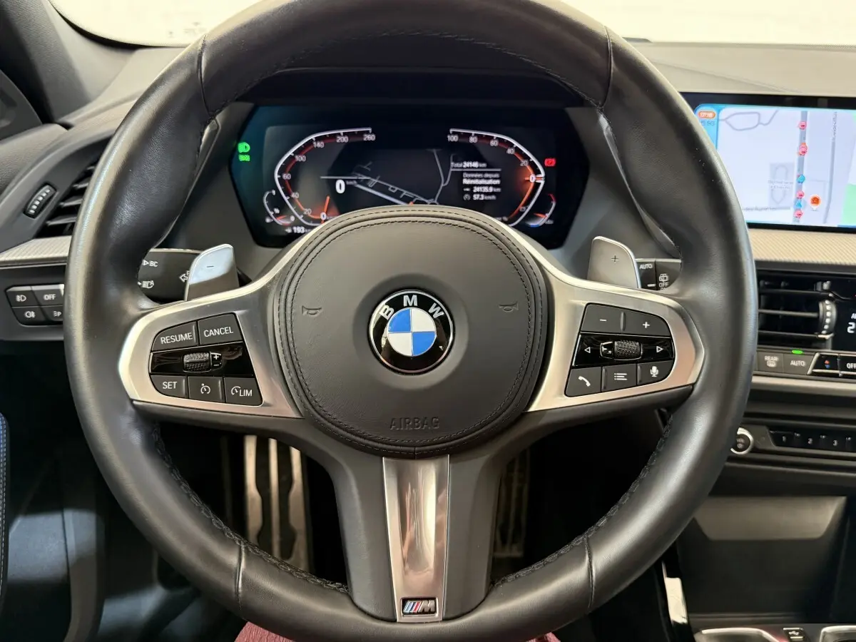Vue rapprochée du volant cuir multifonctions BMW Série 1 noir avec tableau de bord numérique et écran tactile de navigation.