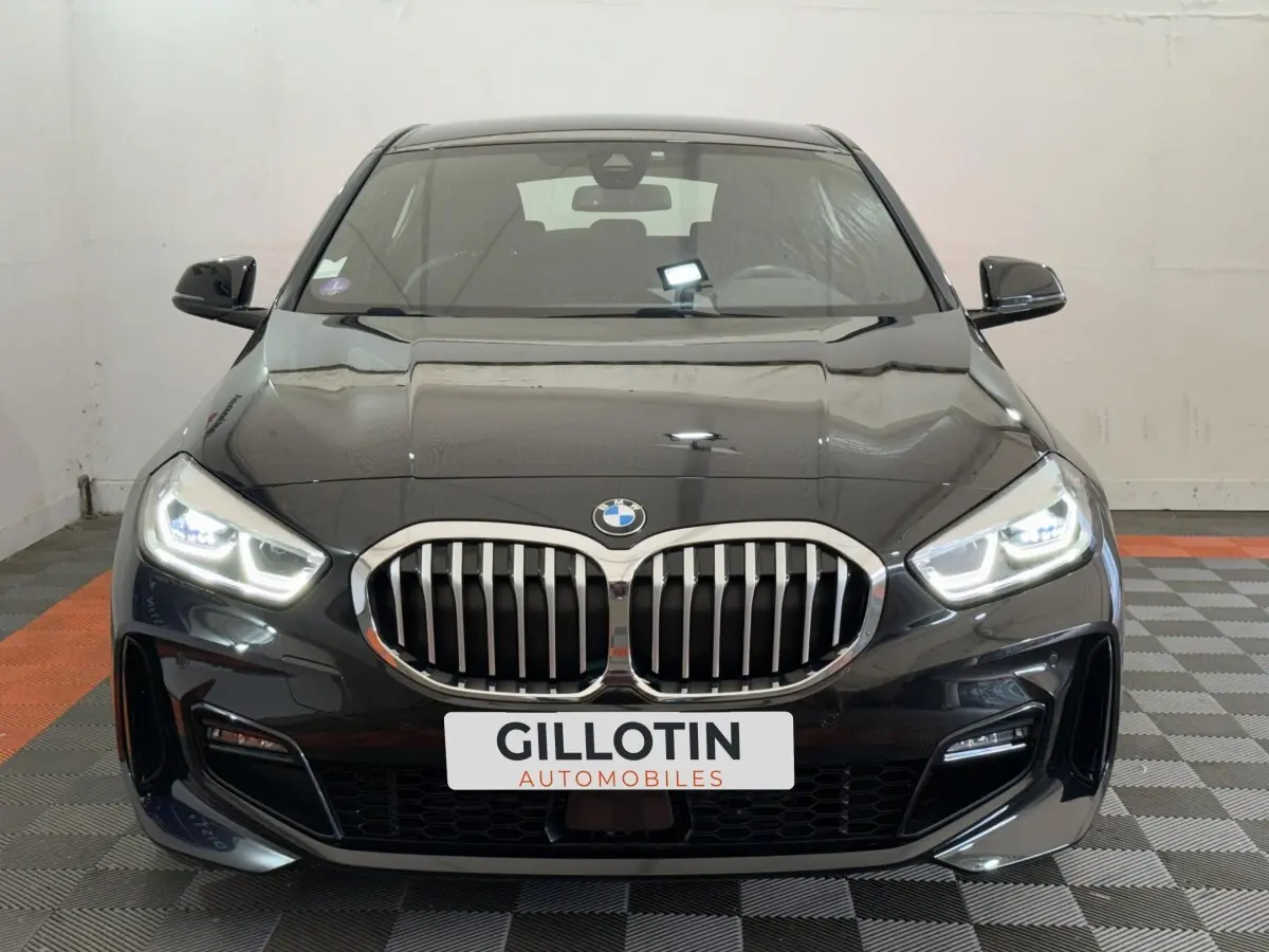 BMW Série 1 120i Edition M Sport Pro noire vue de face avec phares LED allumés et calandre chromée distinctive.