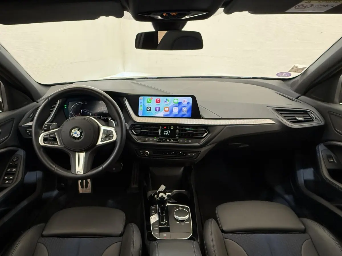 Vue intérieure avant de la BMW Série 1 120i Edition M Sport Pro 2023, tableau de bord noir avec écran tactile central.
