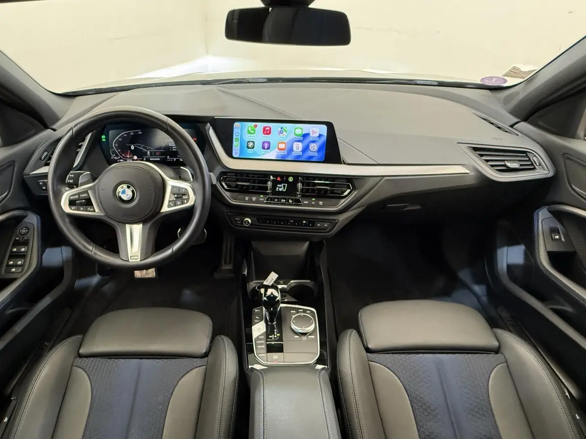 Vue intérieure avant de la BMW Série 1 120i Edition M Sport Pro 2023, tableau de bord et volant cuir noir.
