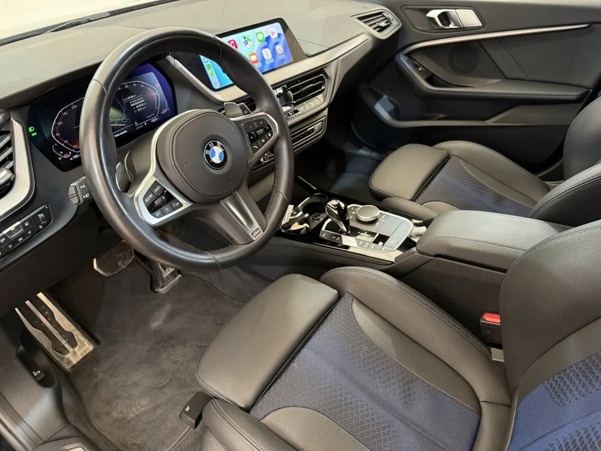 Vue intérieure côté conducteur de la BMW Série 1 120i noire, avec volant cuir multifonctions et écran tactile central.