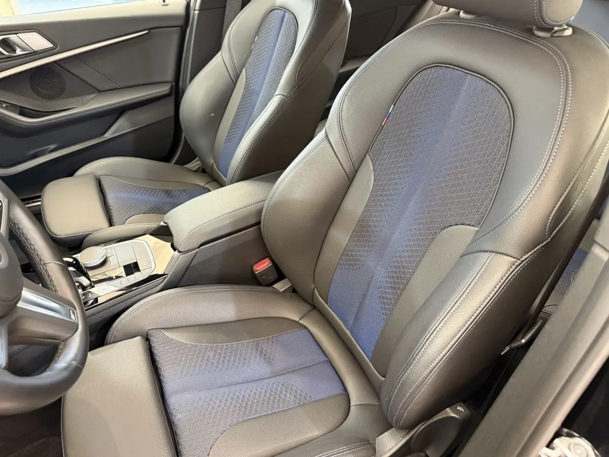 Vue intérieure rapprochée des sièges avant en cuir noir et tissu bleu de la BMW Série 1 120i Edition M Sport Pro.