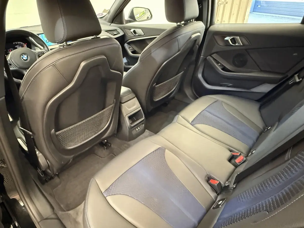 Vue intérieure arrière côté droit de la BMW Série 1 120i noire, montrant la banquette 3 places et les sièges avant en cuir.