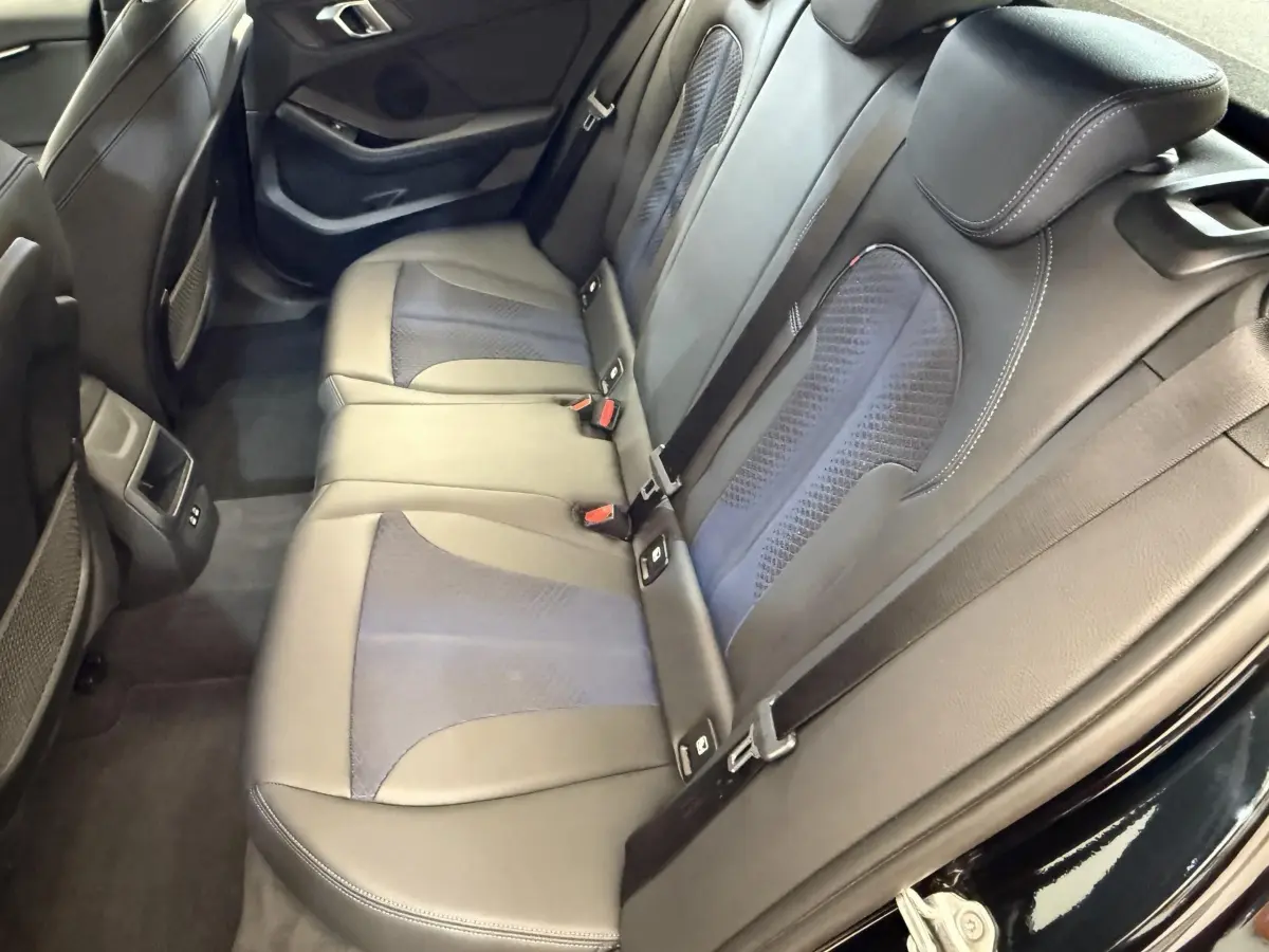 Vue intérieure arrière montrant la banquette 3 places en cuir noir avec inserts tissu sur une BMW Série 1 120i Edition M Sport Pro.