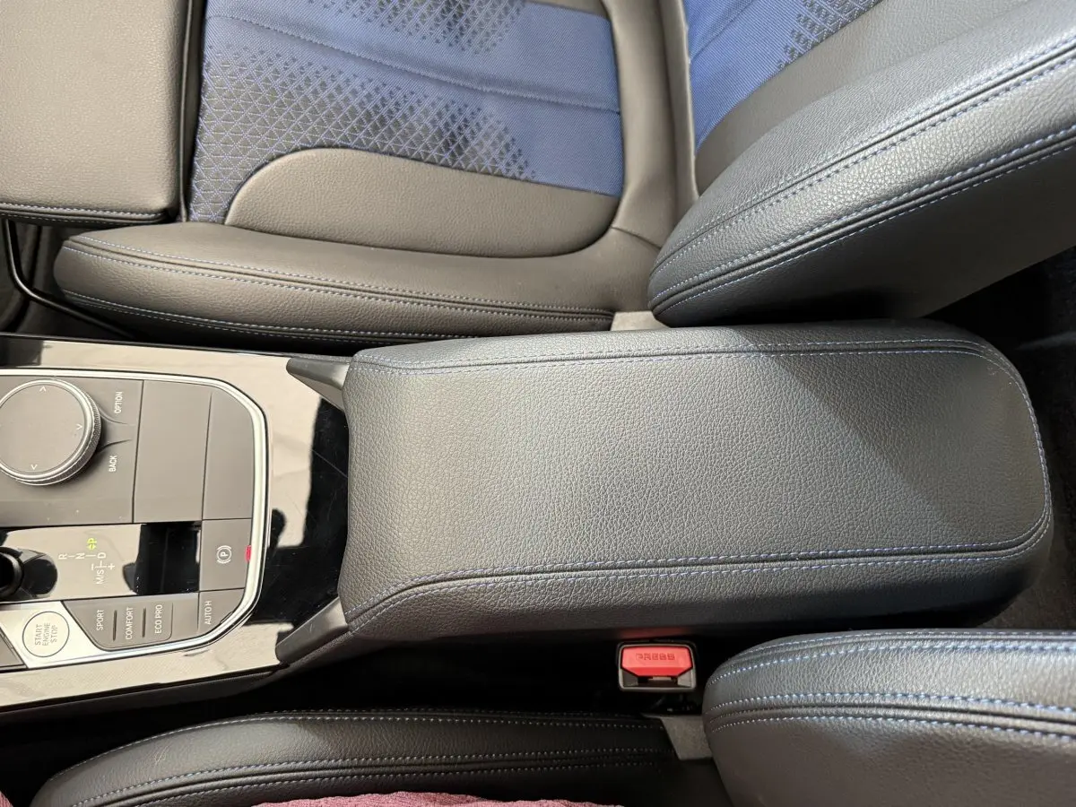 Vue rapprochée de l'accoudoir central en cuir noir et des sièges tissu bleu et cuir noir dans une BMW Série 1.