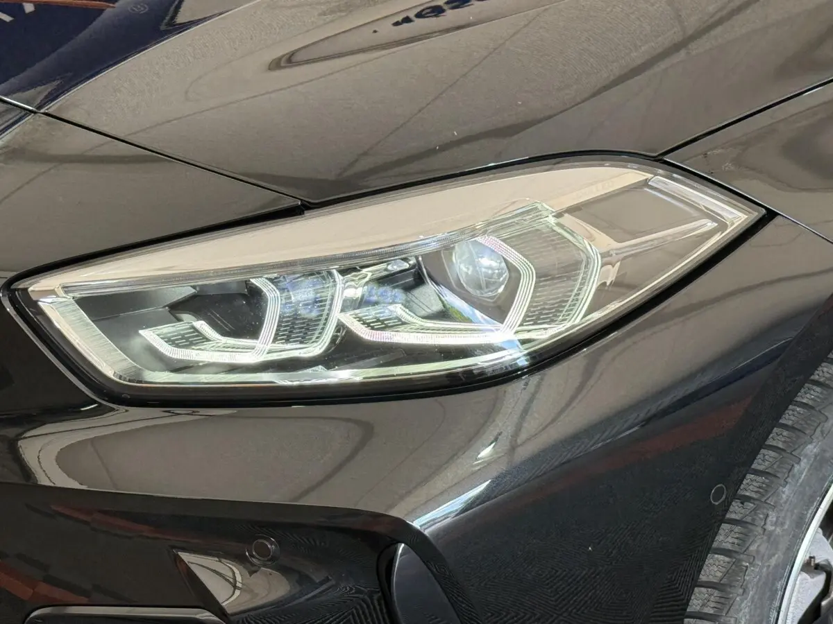 Gros plan sur le phare avant droit LED d’une BMW Série 1 noire, soulignant les lignes modernes et précises du véhicule.