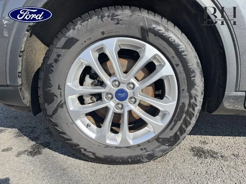 Gros plan sur la jante alu argentée et le pneu du Ford Kuga gris Magnetic, avec logo Ford au centre.