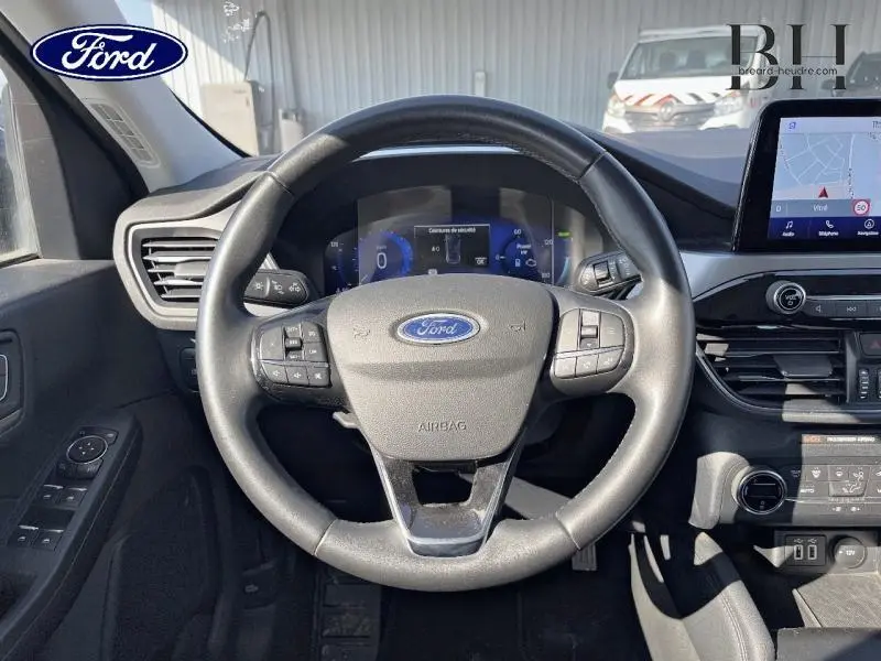 Vue centrée sur le volant cuir multifonction d'une Ford Kuga 2022, avec tableau de bord numérique et écran tactile GPS visible.