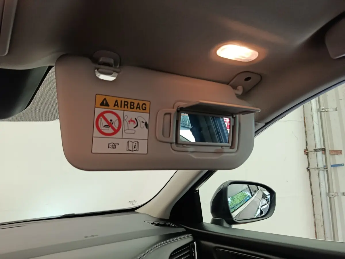 Détail intérieur du pare-soleil côté conducteur avec miroir et avertissement airbag, rétroviseur extérieur noir visible.