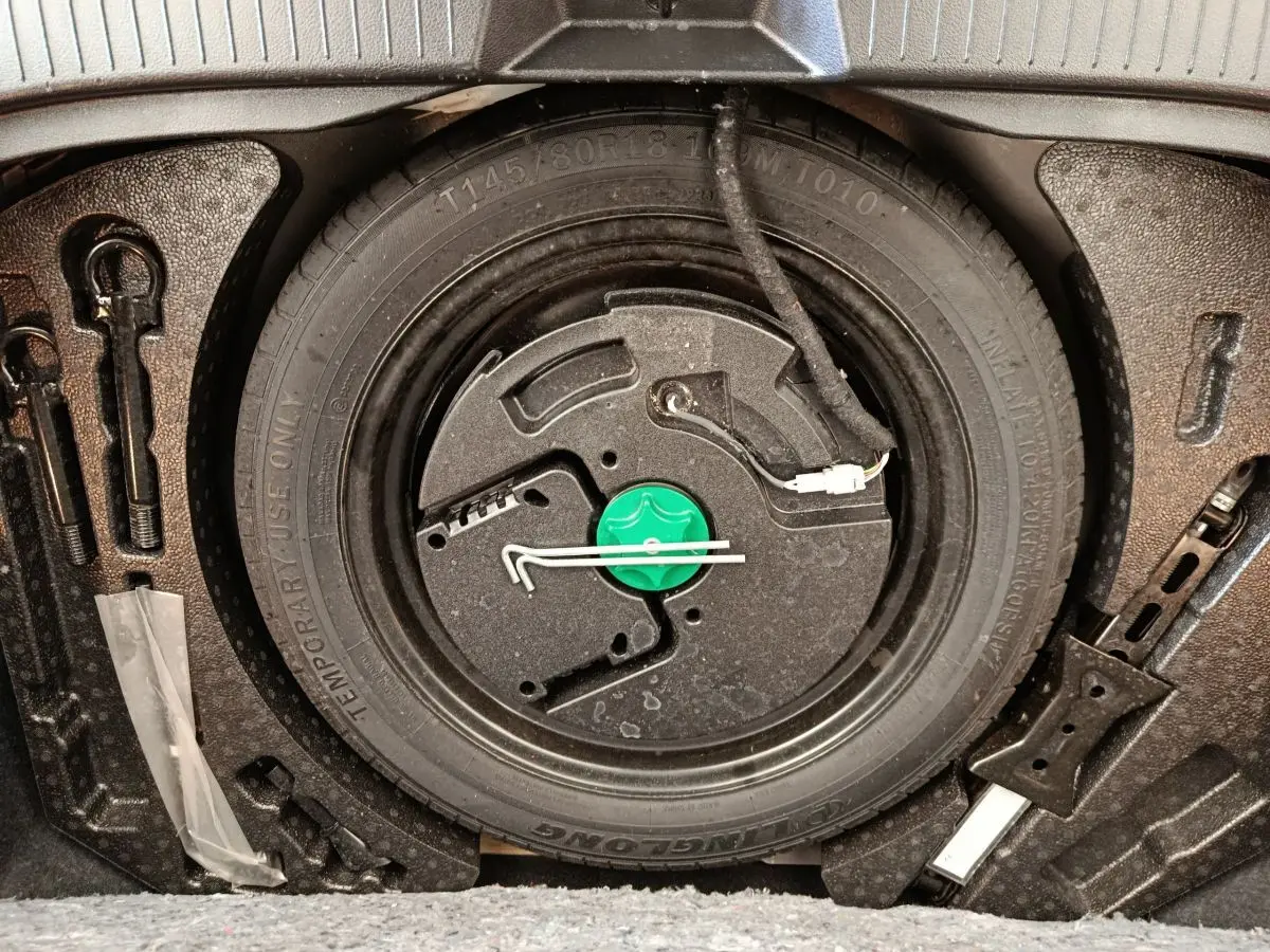 Gros plan sur la roue de secours galette noire et ses outils dans le coffre du Nissan Qashqai e-Power 2024.