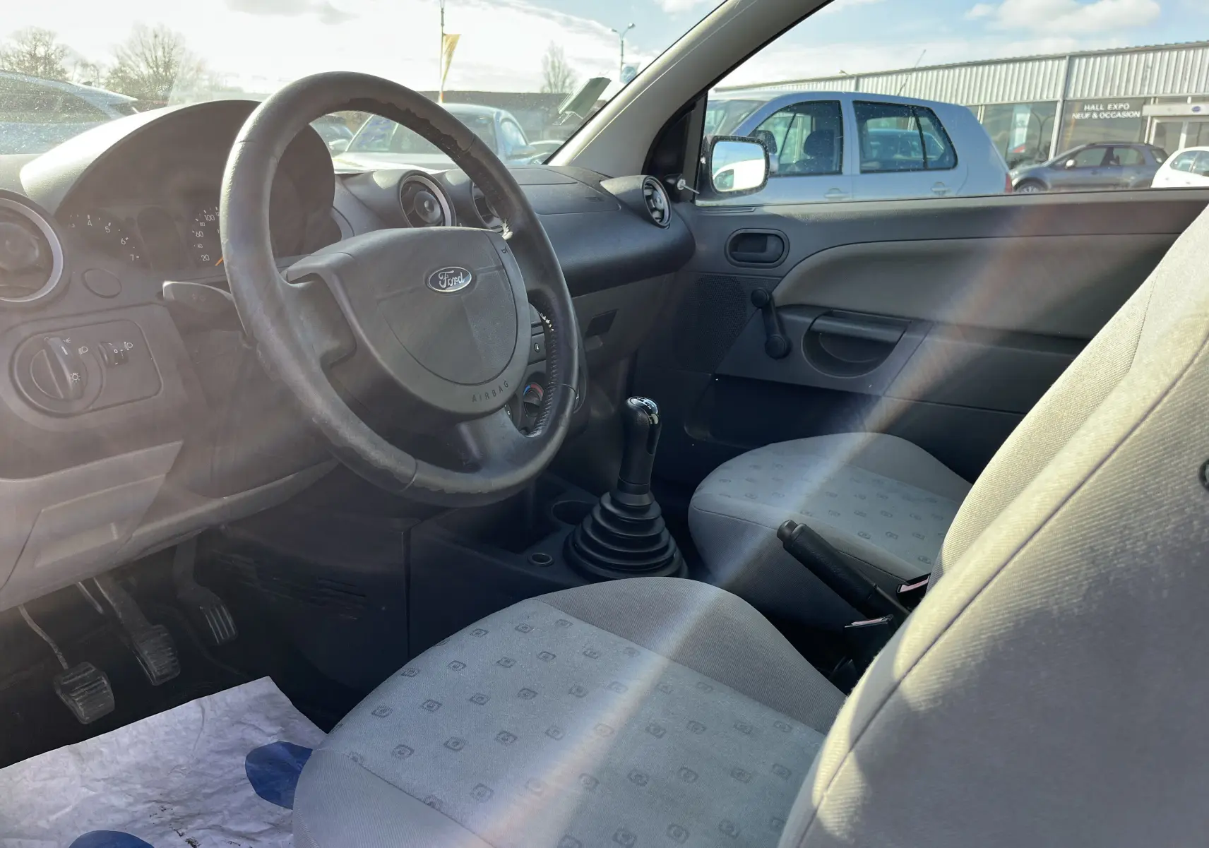 Intérieur de la Ford Fiesta 2003, vue côté conducteur, volant avec logo Ford et levier de vitesse manuel visible.