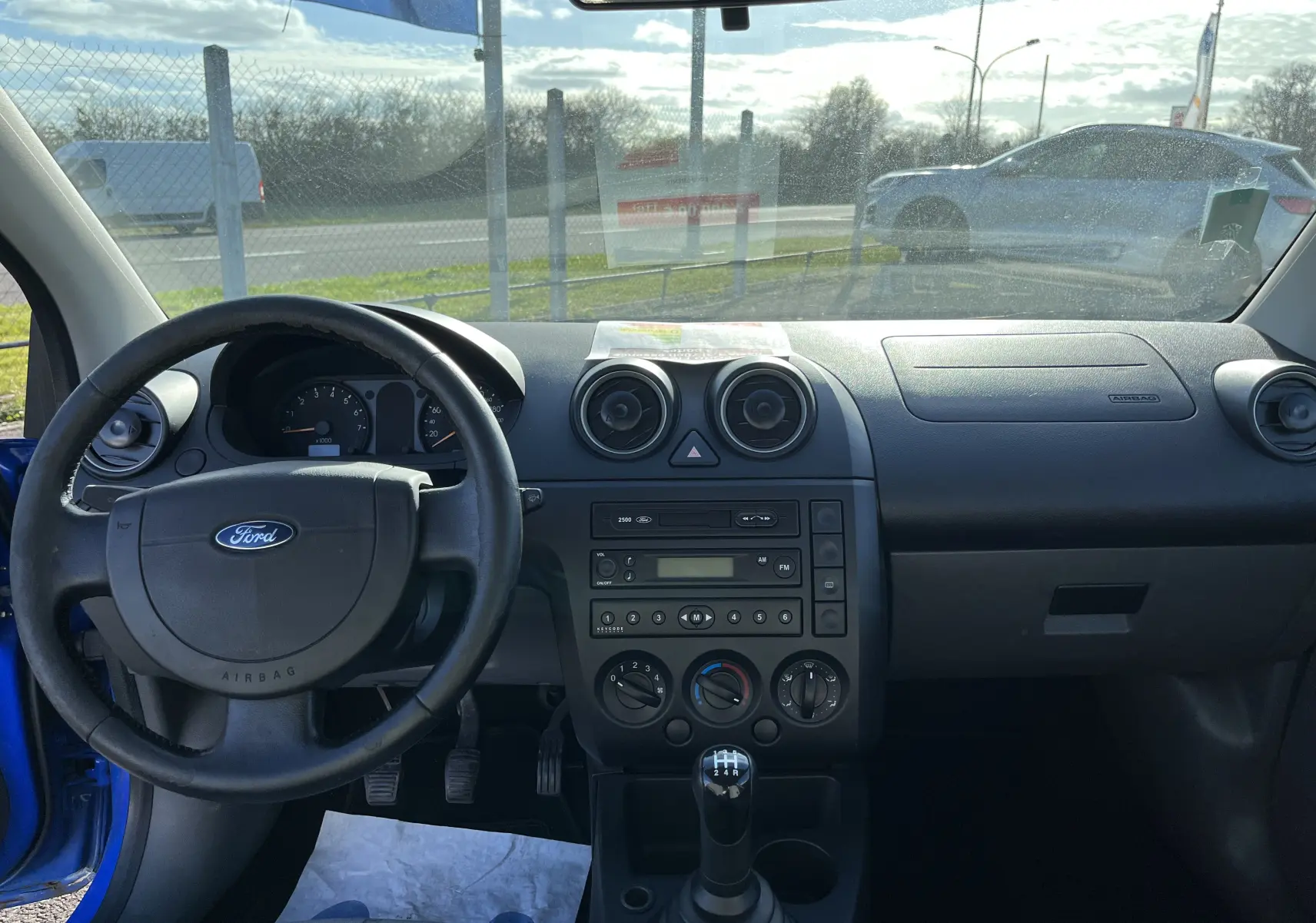 Intérieur d'une Ford Fiesta 2003 bleu, vue de face sur le tableau de bord et levier de vitesses manuel.