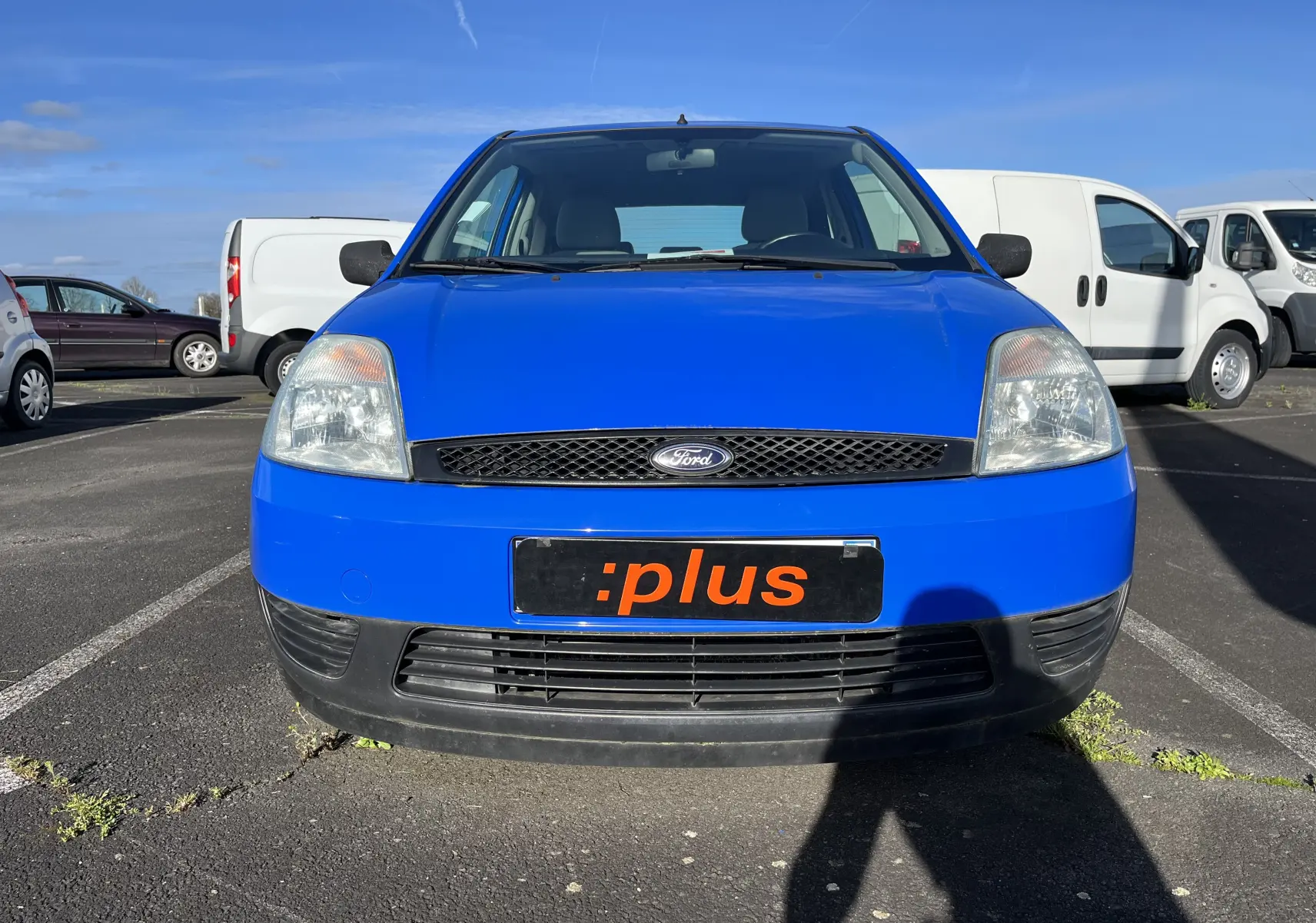 Vue frontale d'une Ford Fiesta bleue 3 portes de 2003, avec calandre noire et plaque d'immatriculation personnalisée.