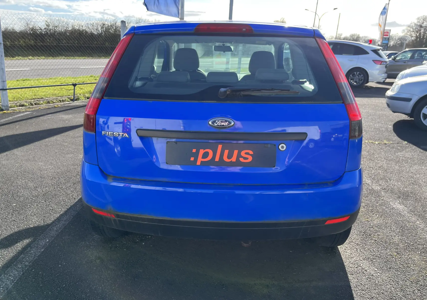 Vue arrière d'une Ford Fiesta bleue 3 portes de 2003, avec logo Ford et plaque d'immatriculation personnalisée :plus.