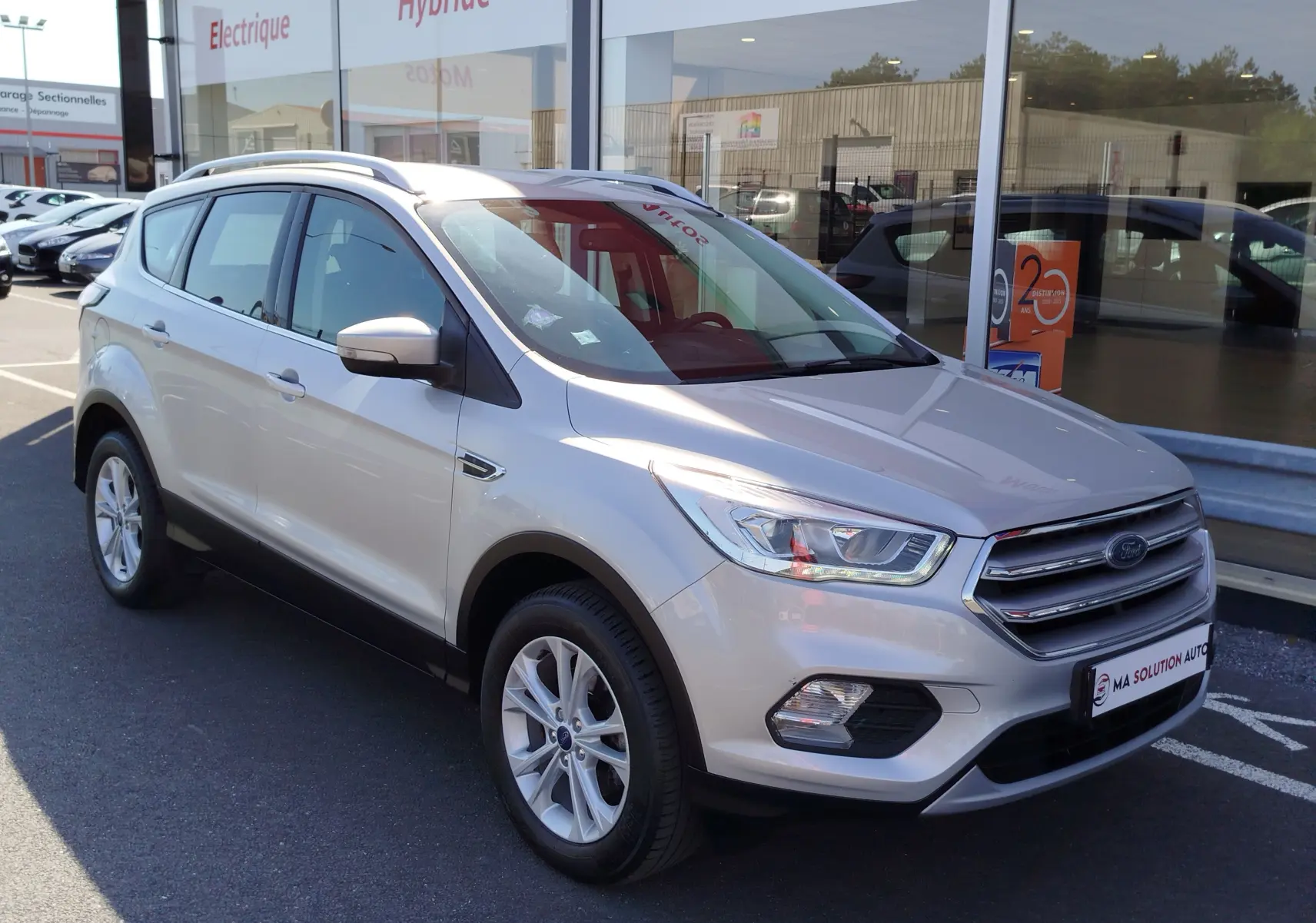 Ford Kuga gris clair vu en 3/4 avant droit, avec calandre chromée et jantes alliage 17 pouces.