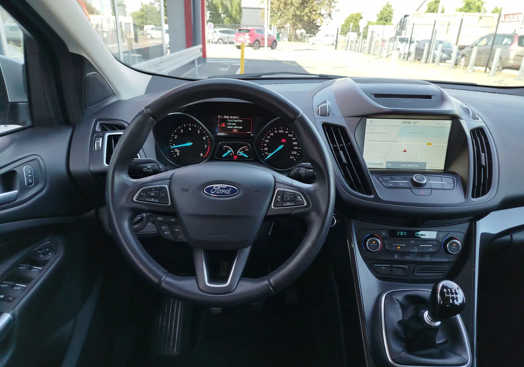 Vue intérieure du tableau de bord du Ford Kuga 2019, volant cuir, écran tactile et levier de vitesse manuel visibles.