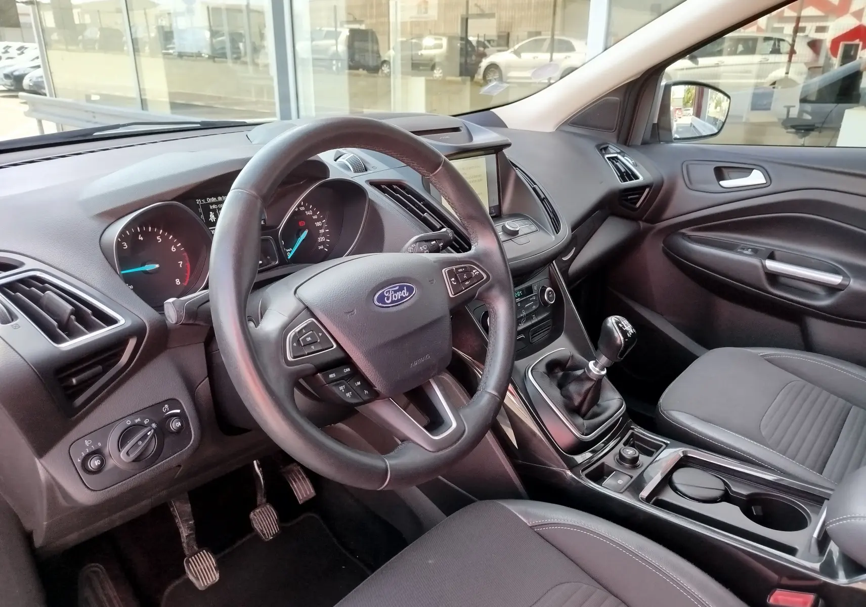 Intérieur du Ford Kuga 2019 vu côté conducteur, volant cuir, tableau de bord avec écran central et boîte manuelle.