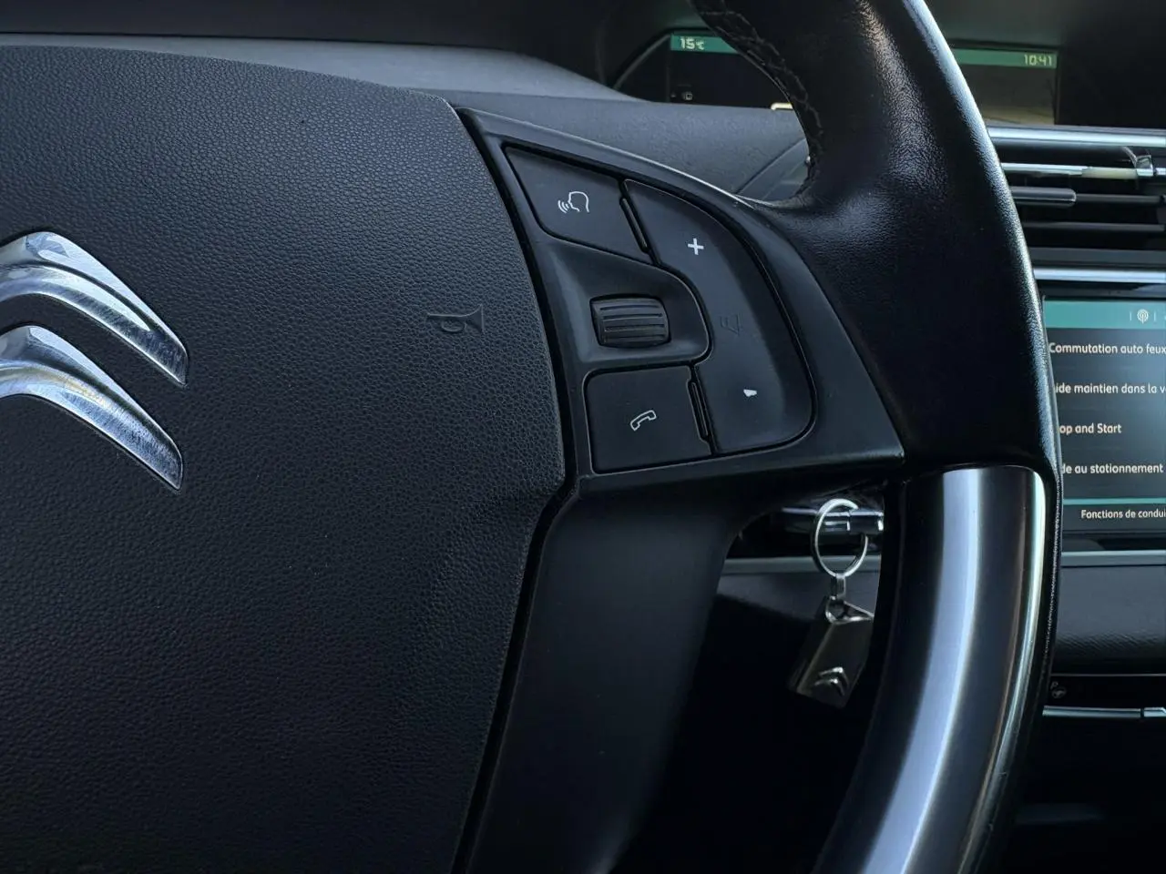 Gros plan sur le volant cuir noir de la Citroën C4 Picasso 2017 avec commandes intégrées et clé insérée au contact.