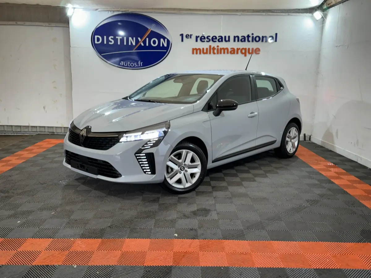 Renault Clio gris clair vue 3/4 avant droit, avec feux LED allumés dans un showroom multimarque.