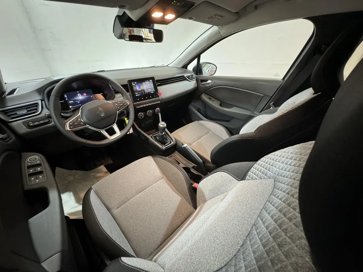 Intérieur de Renault Clio Evolution Blue dCi 100 2025, vue côté conducteur, sièges gris clair et tableau de bord moderne.