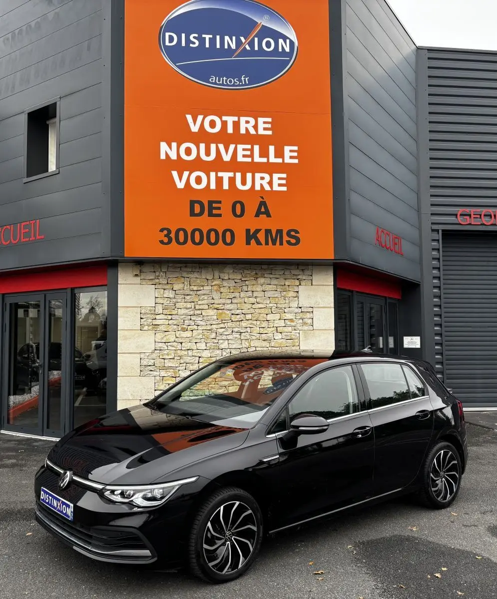 Volkswagen Golf noire vue en 3/4 avant droit, stationnée devant un bâtiment avec panneau orange Distinxion.