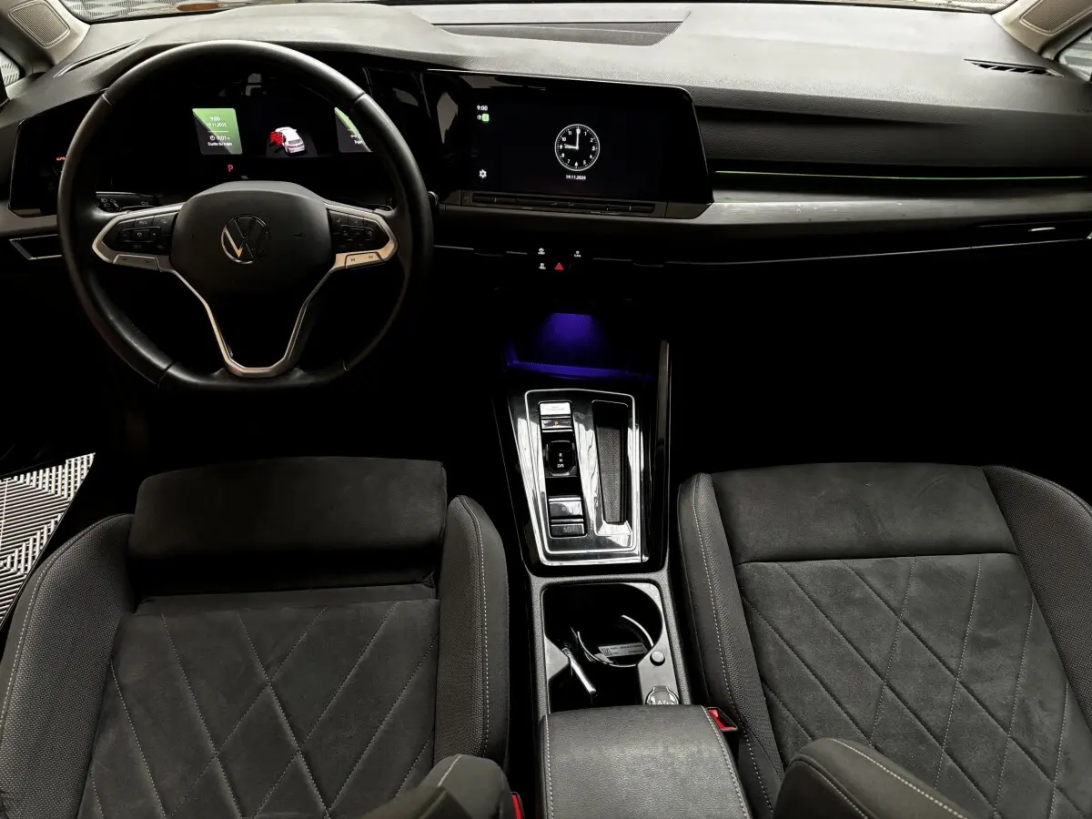 Vue intérieure avant de la Volkswagen Golf noire 2024, volant cuir, écran tactile et console centrale moderne éclairée.