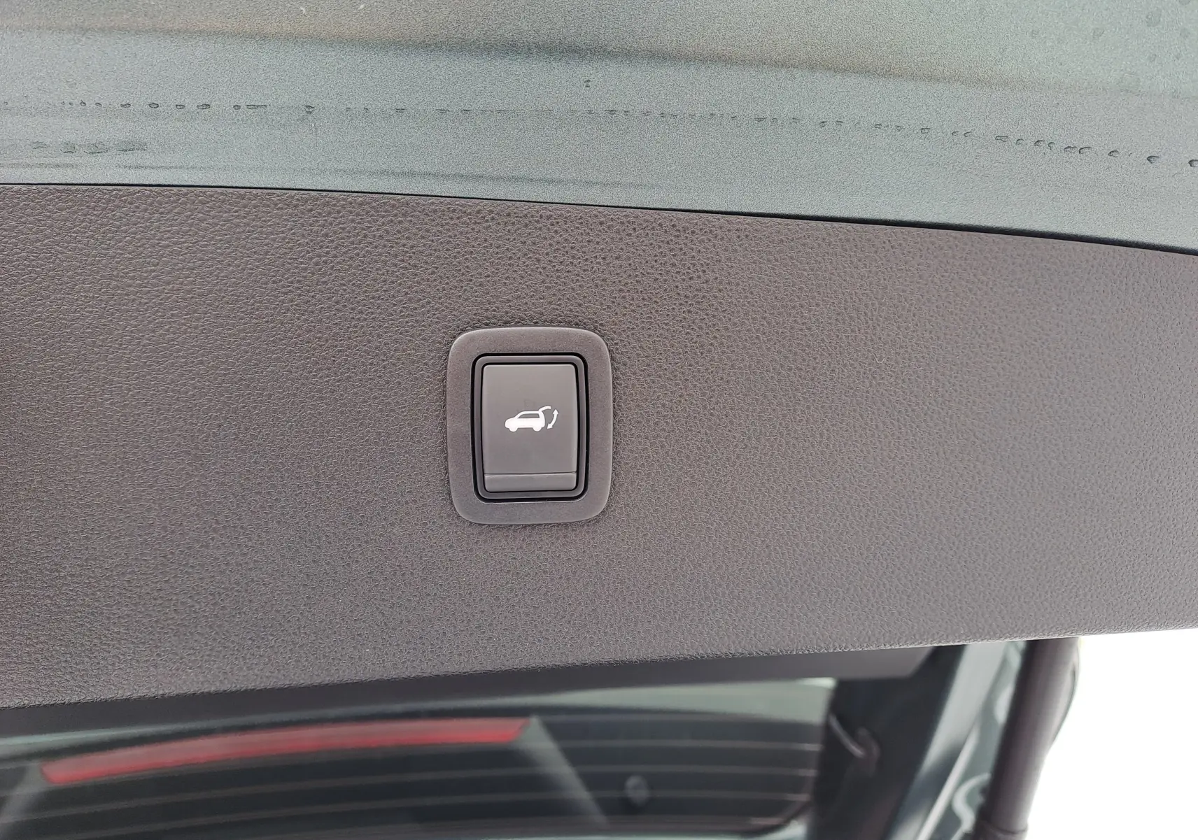 Bouton d'ouverture électrique du coffre sur la partie intérieure du hayon du Dacia Bigster vert cèdre.