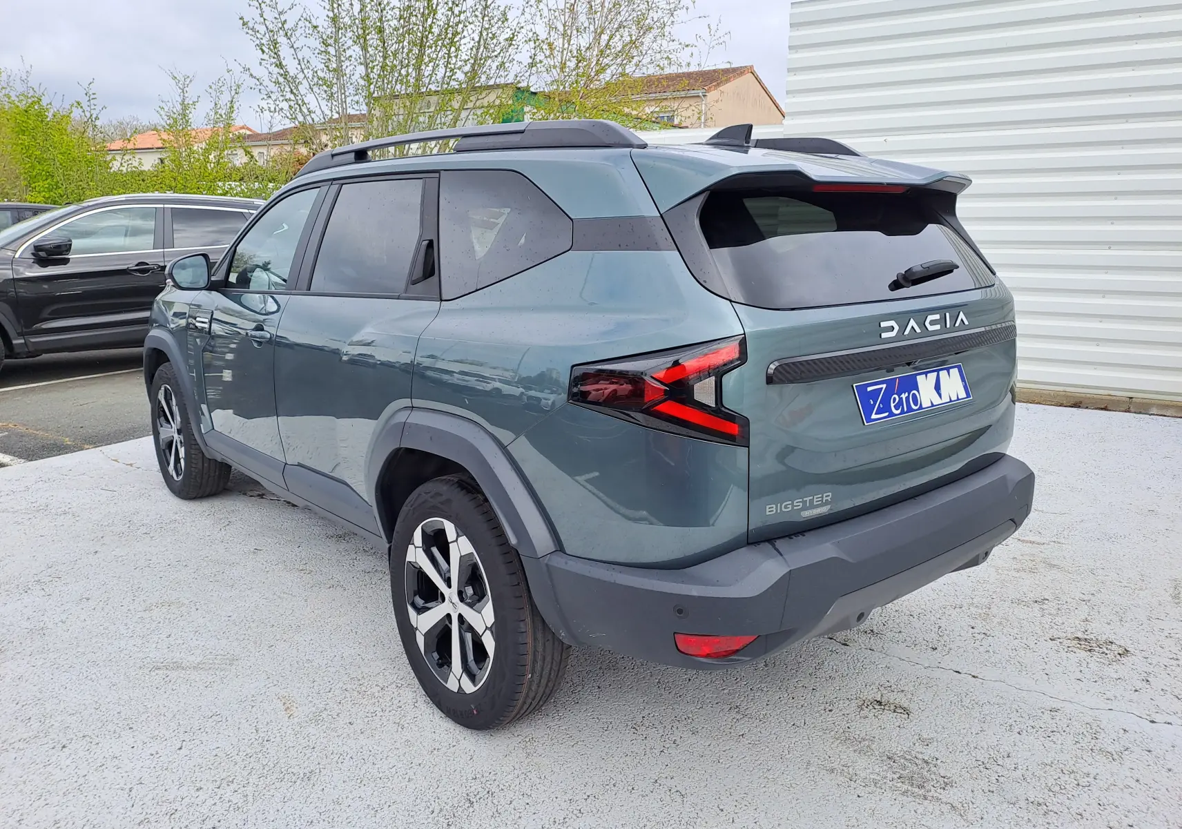 Vue 3/4 arrière droite d'un Dacia Bigster vert cèdre avec détails noirs et jantes bicolores sur parking.