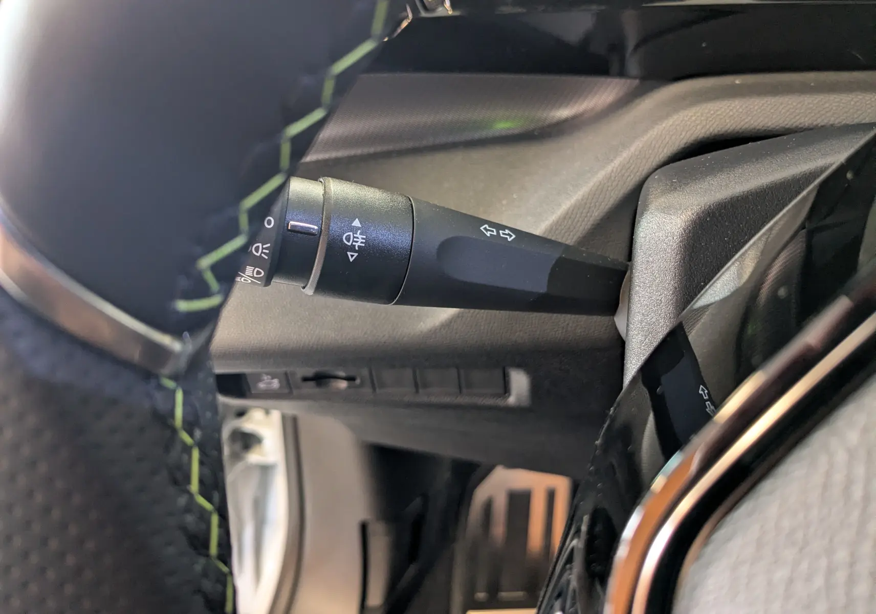 Gros plan sur la manette de clignotant à gauche du volant avec surpiqûres vertes dans l’habitacle noir du Peugeot 408 Hybrid 2025.
