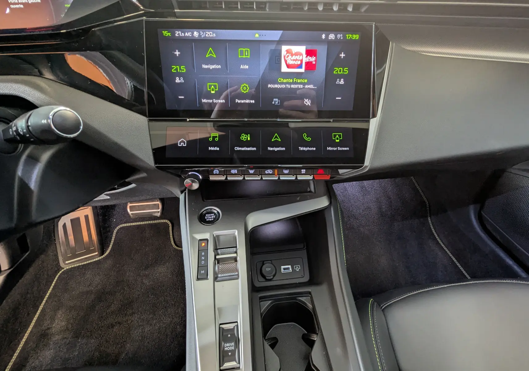 Vue intérieure centrée sur la console centrale et l’écran tactile du Peugeot 408 Hybrid blanc Okenite, avec commandes et pédales visibles.