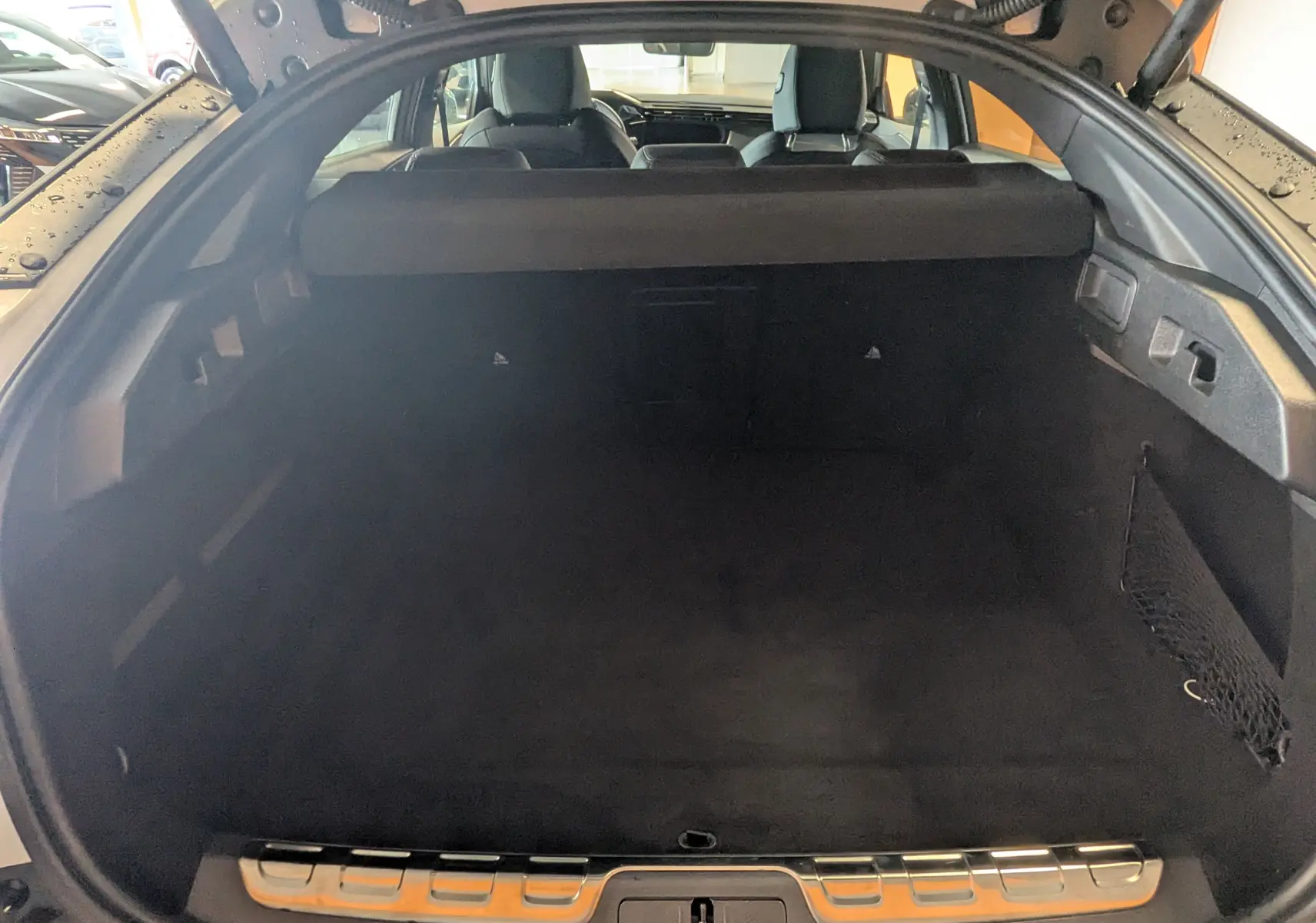 Coffre ouvert vu de l'arrière d'une Peugeot 408 Hybrid 145 e-DCS6 GT blanc Okenite, intérieur noir et filet latéral.