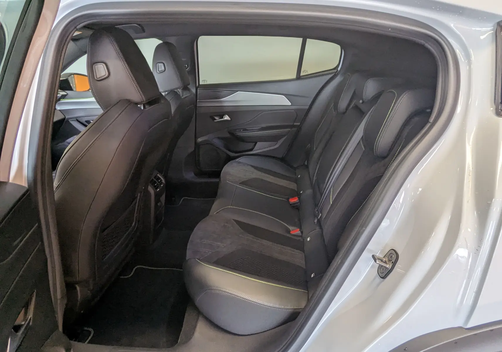 Vue côté droit de l'intérieur arrière du Peugeot 408 blanc Okenite, sièges noirs avec surpiqûres vertes et vitres surteintées.