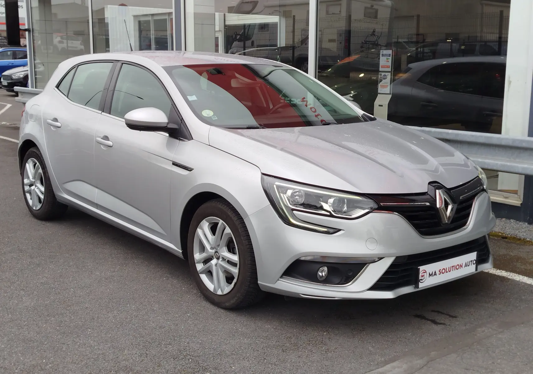 Renault Mégane gris titanium vue 3/4 avant droit, avec phares LED et jantes alliage visibles.