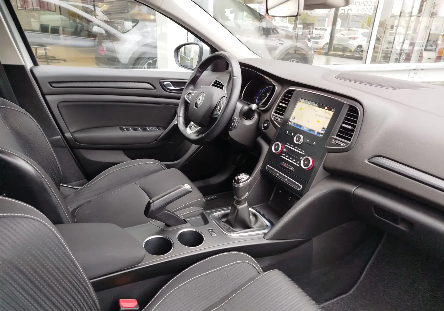Vue intérieure côté conducteur de la Renault Mégane gris Titanium, montrant le tableau de bord et la console centrale avec boîte manuelle.