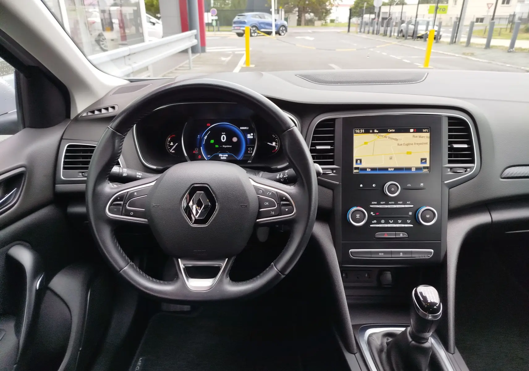 Vue intérieure centrée sur le volant et la console centrale d'une Renault Mégane gris titanium avec boîte manuelle et écran tactile.