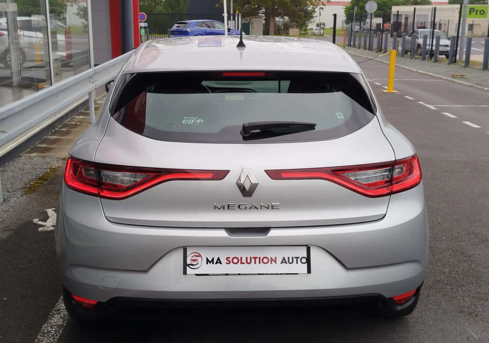 Vue arrière d'une Renault Mégane gris titanium de 2018 avec feux arrière LED allumés, garée en extérieur.
