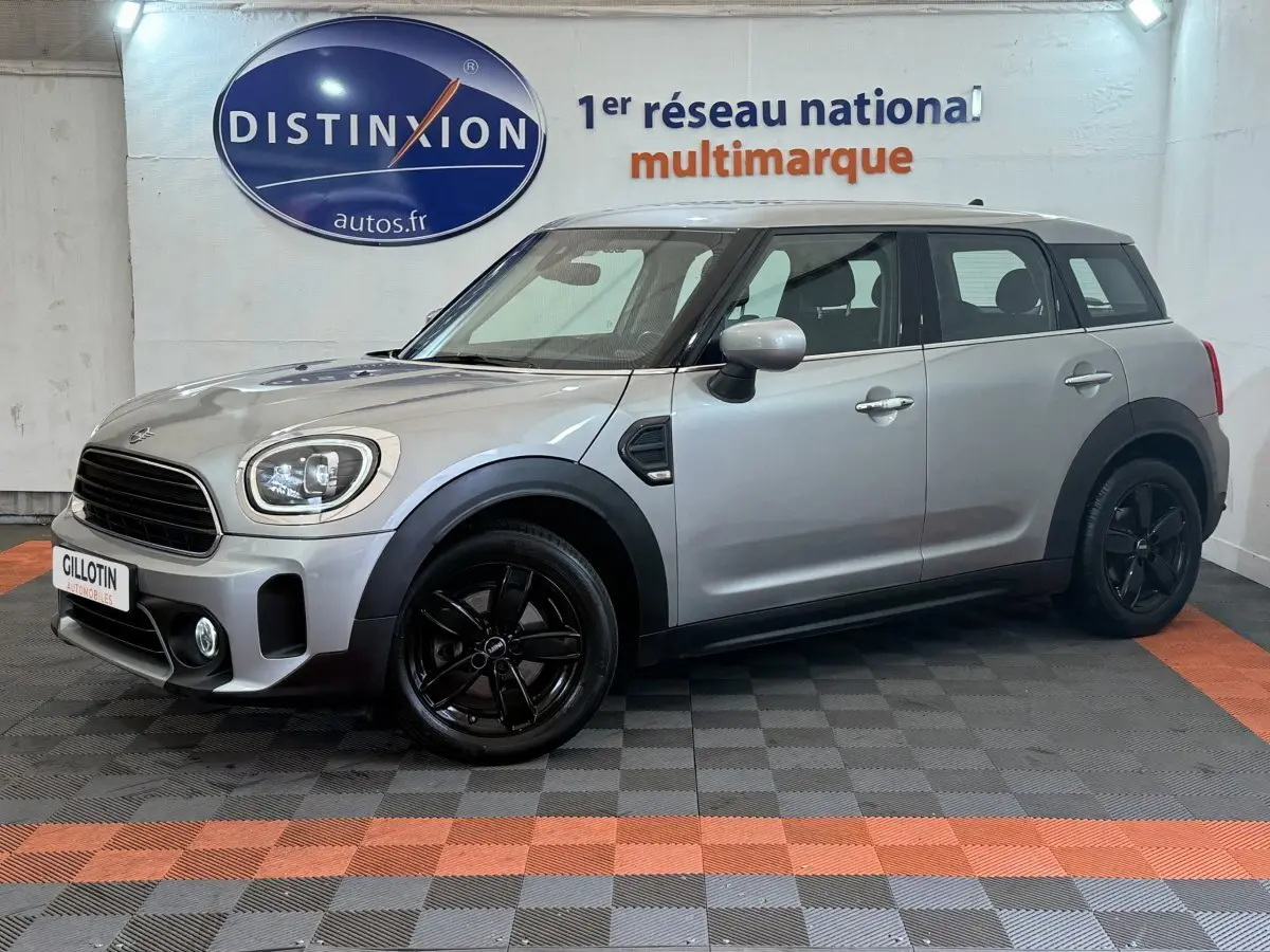 Vue de profil droit d'une MINI Countryman Cooper Essential gris clair avec jantes noires, stationnée en intérieur showroom.