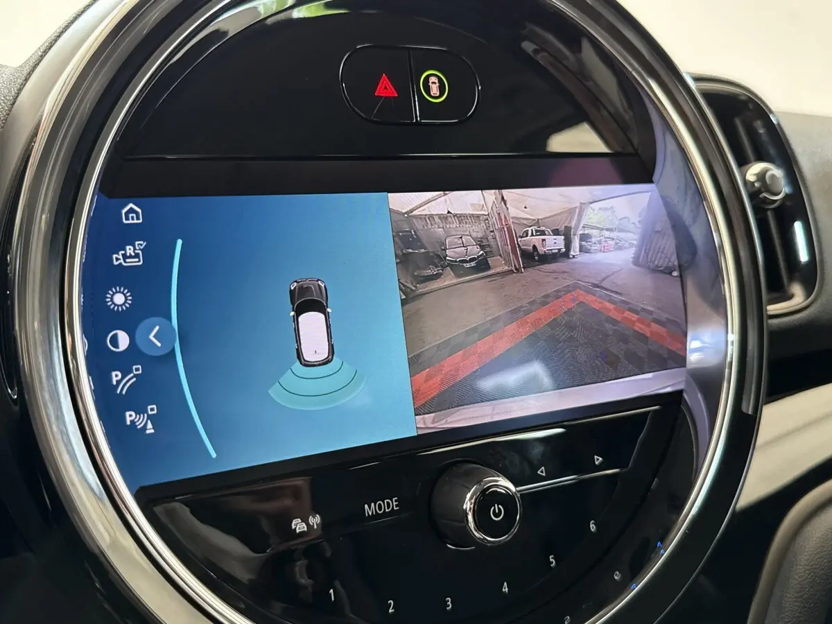 Gros plan sur l'écran tactile central rond du MINI Countryman gris clair, affichant la caméra de recul et les capteurs de stationnement.