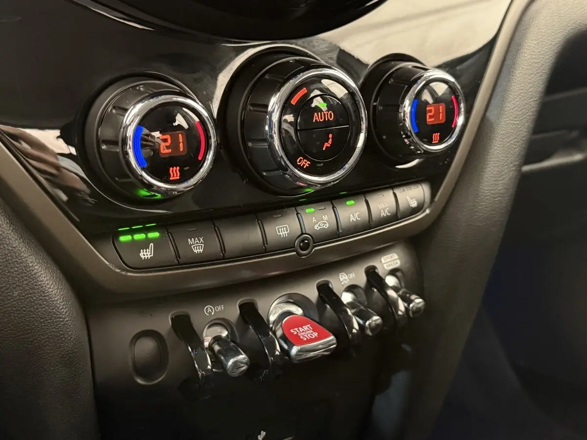 Gros plan sur les commandes de climatisation et le bouton start/stop rouge du tableau de bord noir du MINI Countryman gris clair.