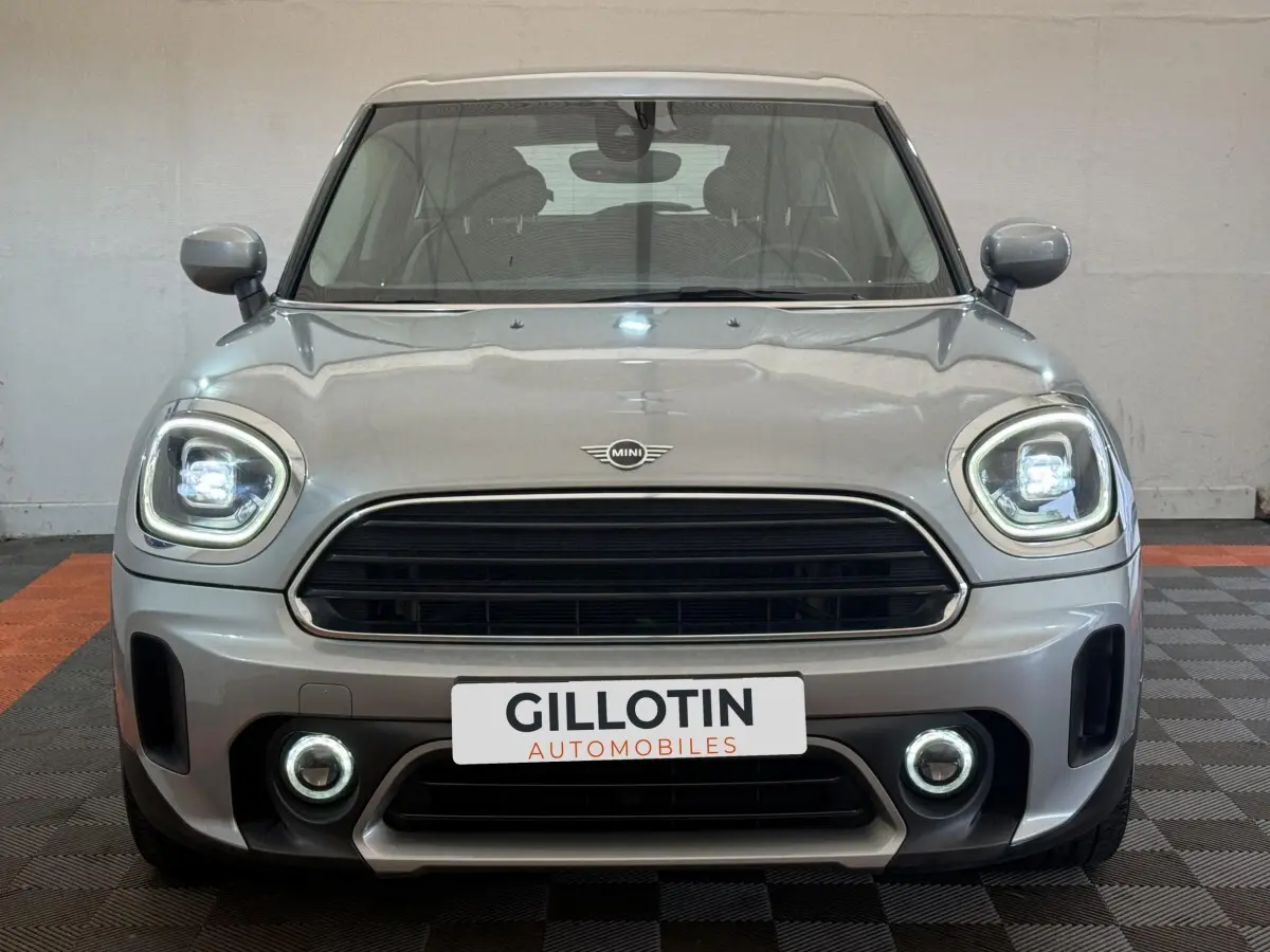Vue avant d'une MINI Countryman gris clair avec phares et antibrouillards LED allumés en intérieur showroom.