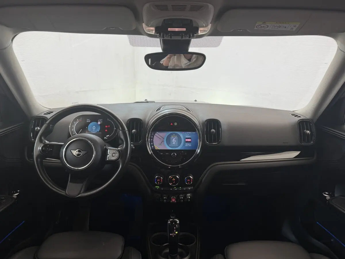Vue intérieure frontale du tableau de bord noir et volant cuir d’une MINI Countryman gris clair 2023 avec écran tactile central rond allumé.