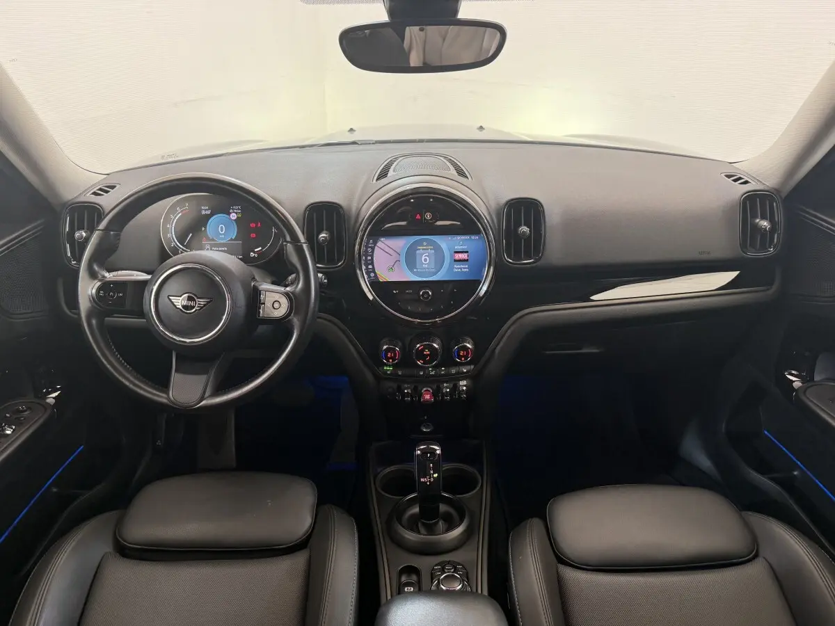 Vue intérieure frontale du tableau de bord noir et volant cuir du MINI Countryman gris clair 2023 avec écran tactile central rond.