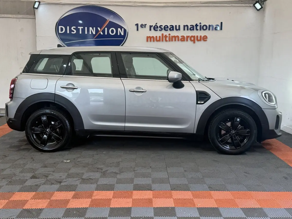 Vue de profil côté gauche d'une MINI Countryman Cooper Essential gris clair avec jantes noires, stationnée en intérieur.